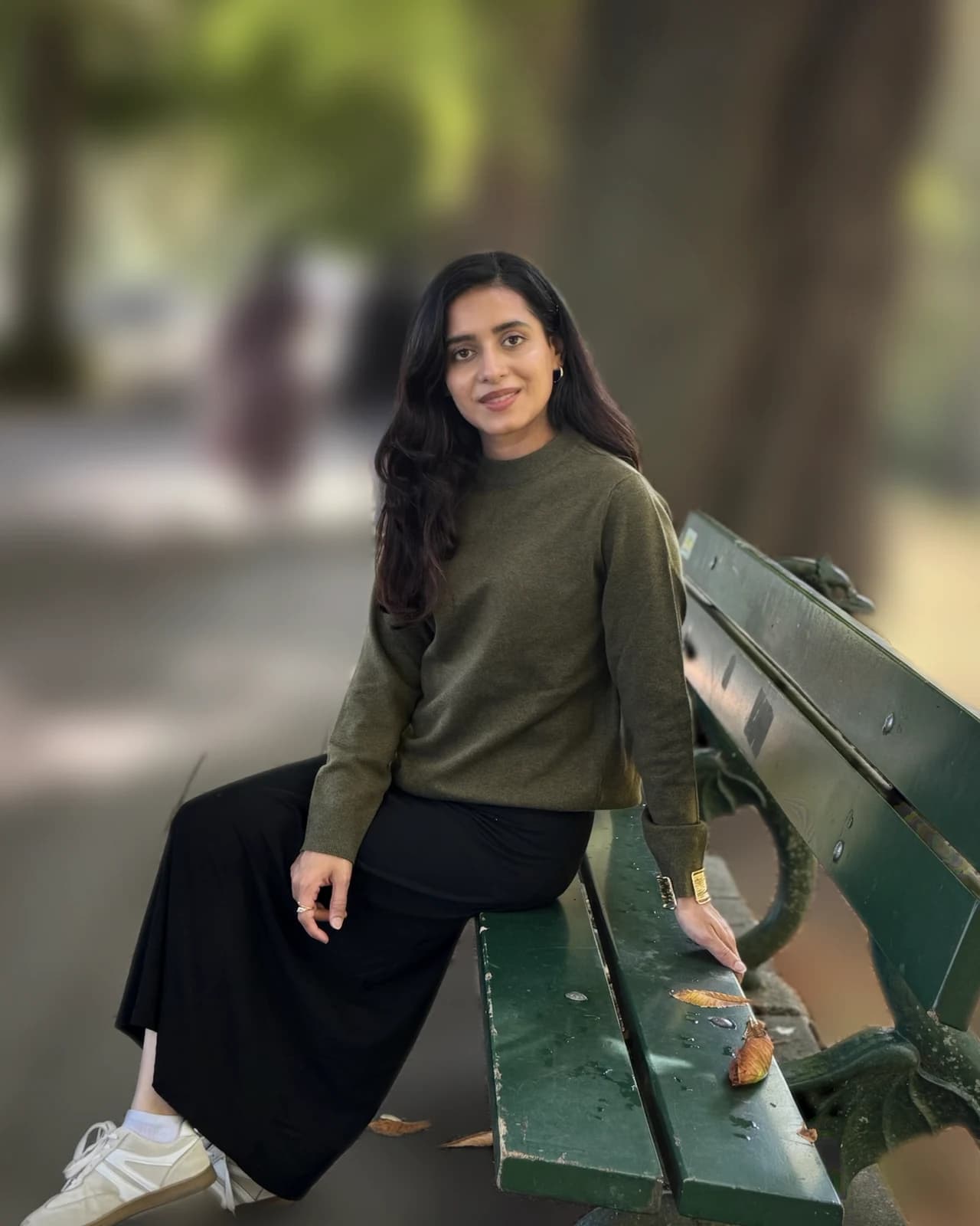 Nimra Zahid seated on a green park bench under autumn trees